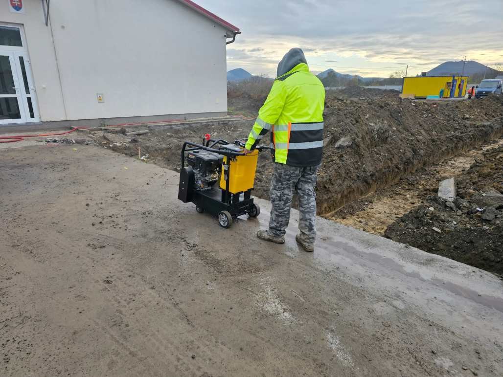 Robotník so strojom na betónovej ploche pri budove