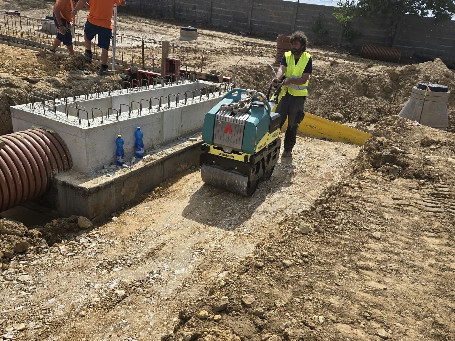 Robotník hutní zásyp vibračným valcom pri betónovej šachte