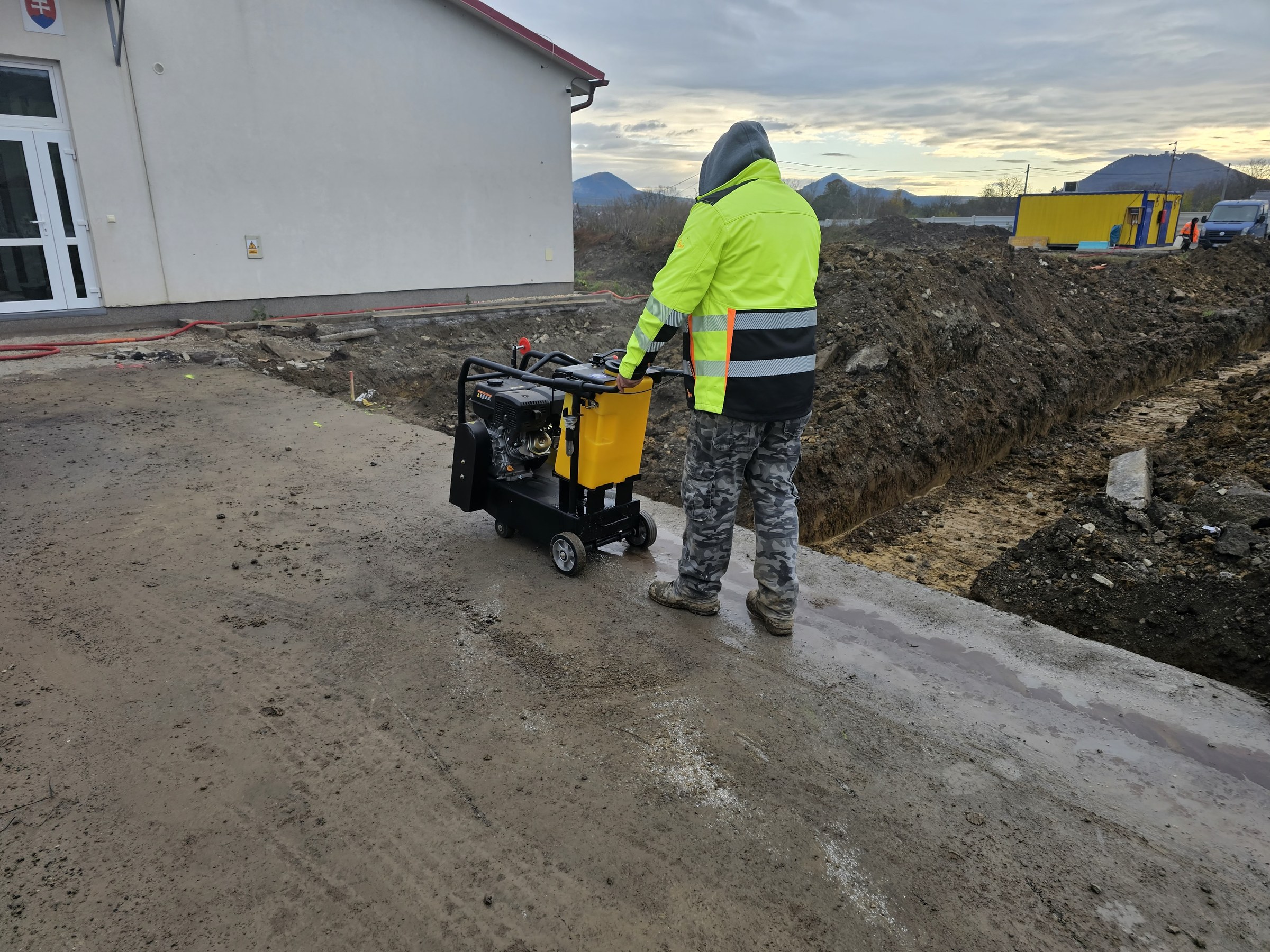 Robotník s vibračnou doskou pri budove školy