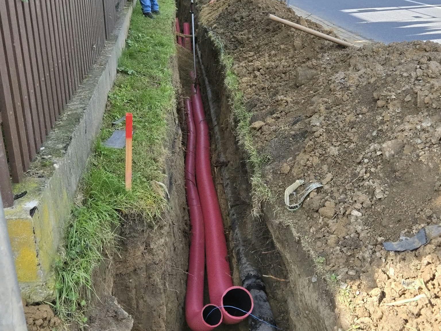 Červené chráničky vo výkope pozdĺž plotu a cesty